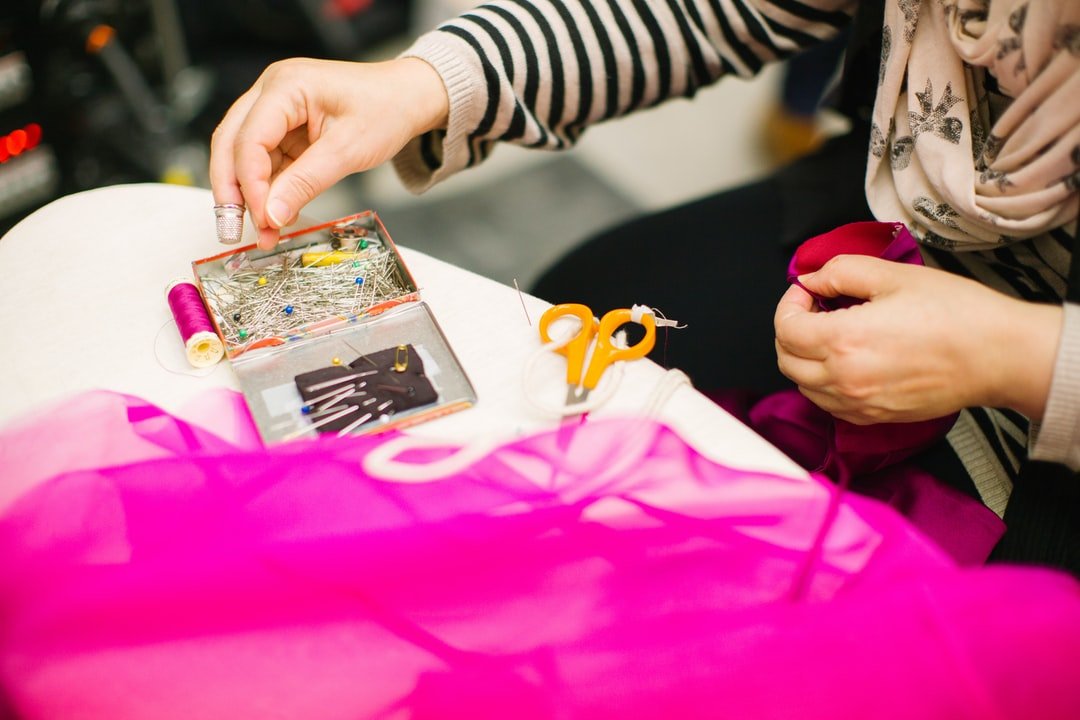 <p>Seamstress hands, sewing bright pink material.</p>